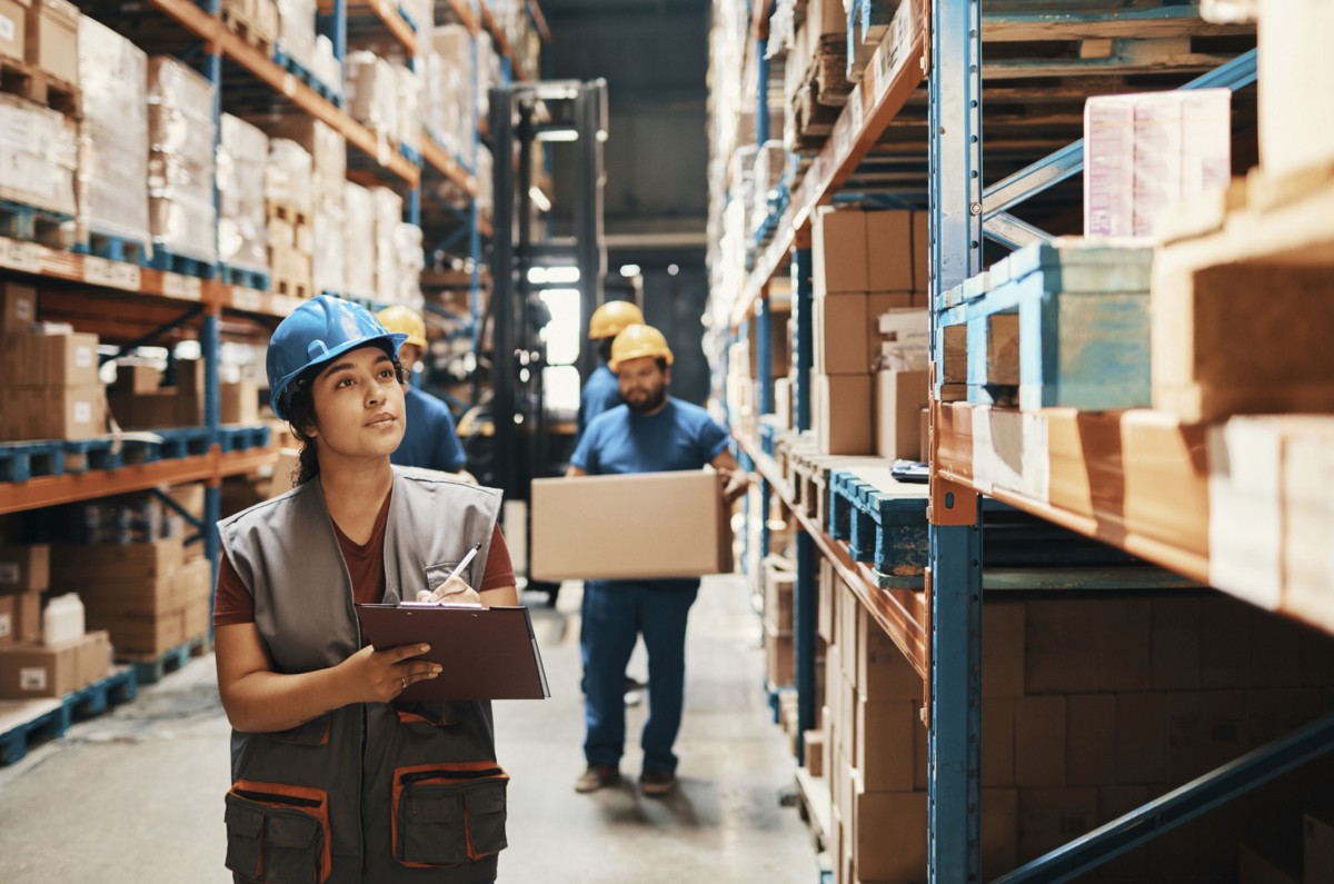 A woman in a warehouse holding a clipboard and making a note of it